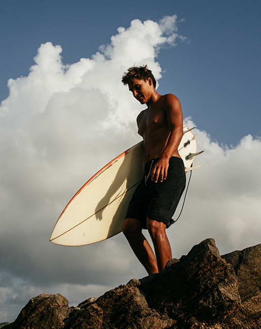 MAN ON ROCK WITH SURFBOARD