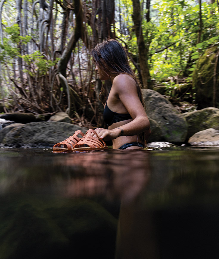 http://Woman%20walking%20in%20stream%20holding%20sandals